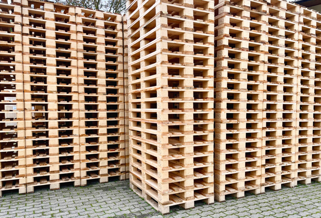 Stosy drewnianych europalet EPAL ustawione na zewnątrz, ułożone w wysokie kolumny na brukowanej powierzchni.